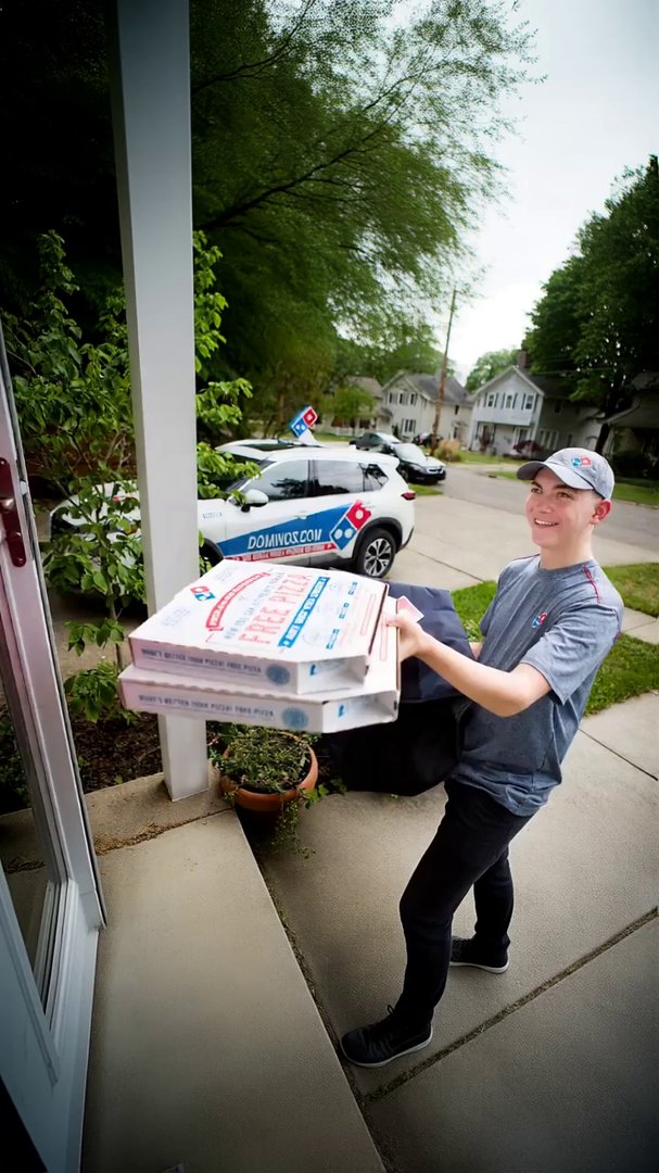 driver smiles and hands customer the pizza, saying...