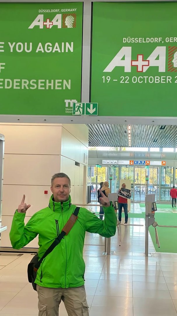 Veo 3.1: Create a short cinematic vertical video (9:16) using a photo taken at the end of a major trade fair.
A confident man in a bright green jacket stands i