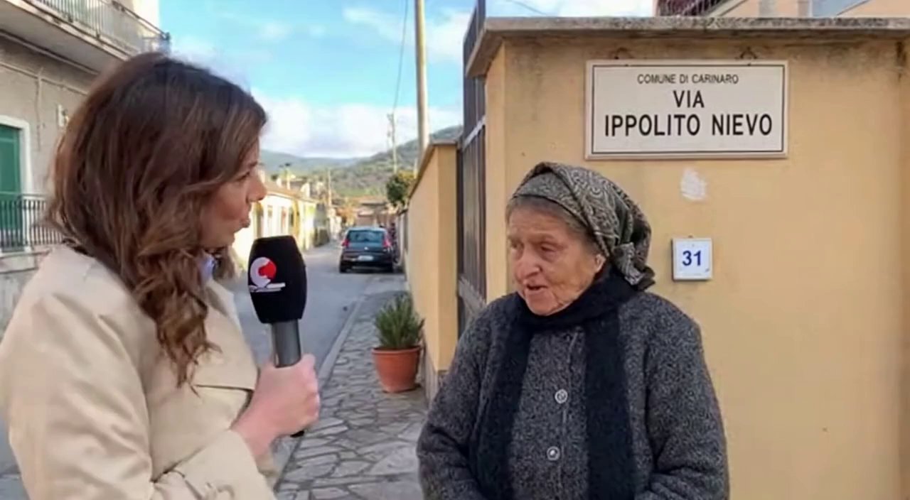[Sora 2] C e la giornalista che incontra una signora anziana davanti al cartello Via Ippolito Nievo nel comun... - Veo 3 AI video prompt thumbnail
