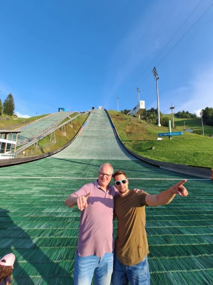 Kling 3.0: Image-to-video, 7–9 seconds, realistic cinematic. Keep the two men’s faces, identity, body shape and outfits exactly the same as in the phot